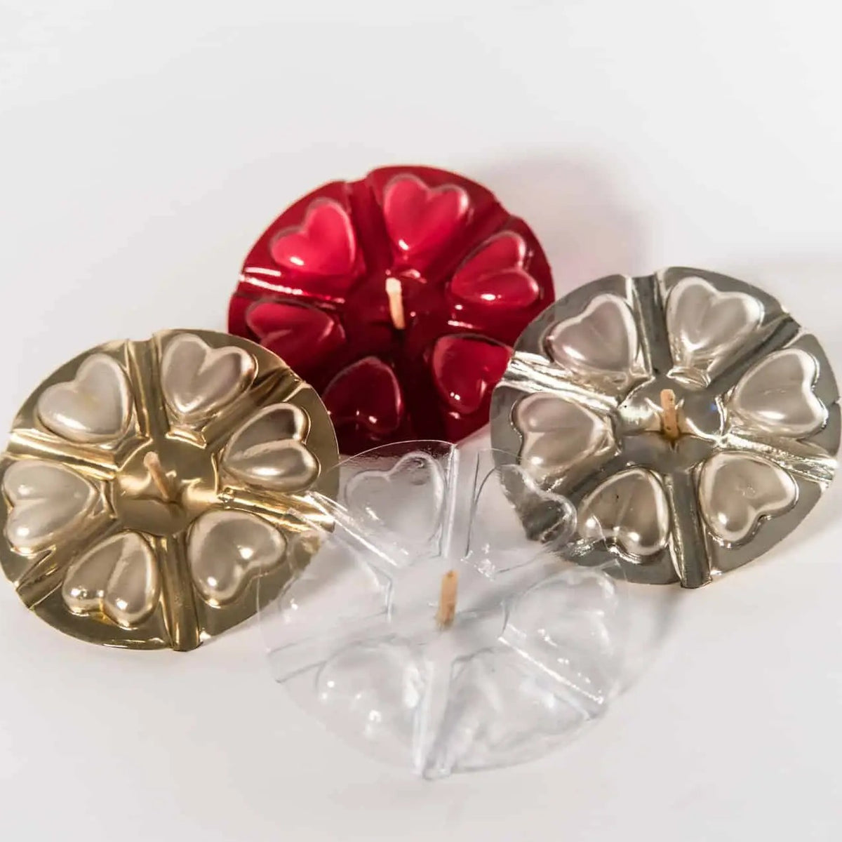 Four candles with heart shared molding in gold, red, and silver, arranged on a plain white background.