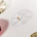 A close-up of an Aromaglow floating candle in a clear, flower-shaped wax on a white surface, with a small wick visible in the center.