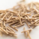 A close-up shot of scattered light brown long-lasting Aromaglow wicks on a plain white background.