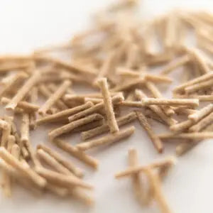 A close-up shot of scattered light brown long-lasting Aromaglow wicks on a plain white background.