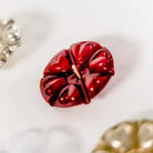 A glossy red flower-shaped Aromaglow candle with a central wick, displayed on a white surface with other decorative items partially visible in the corners.