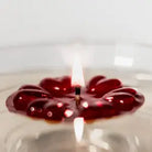 A red Aromaglow floating candle in the shape of a flower, lit with a small flame in the center, set against a soft, out-of-focus light background.